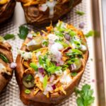 Close-up of buffalo chicken stuffed sweet potato topped with ranch, red onion, jalapeños, and cilantro.