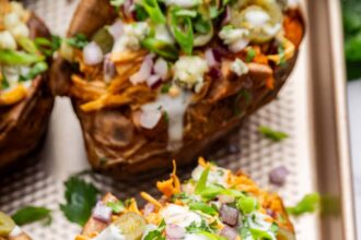 Close-up of buffalo chicken stuffed sweet potato topped with ranch, red onion, jalapeños, and cilantro.
