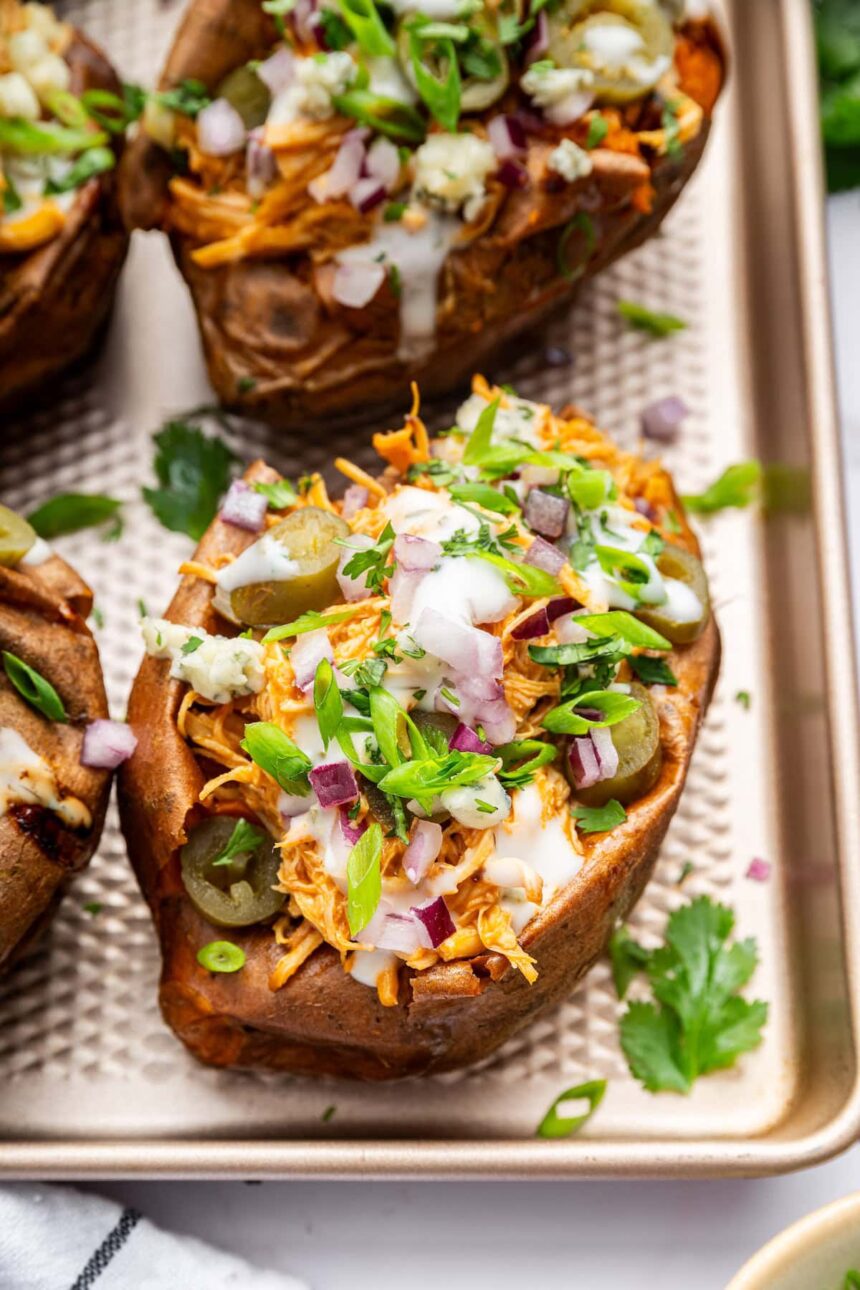 Close-up of buffalo chicken stuffed sweet potato topped with ranch, red onion, jalapeños, and cilantro.