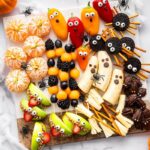 Halloween snack board featuring fruit kabobs, apple monster mouths, banana ghosts, Oreo spiders, and clementine pumpkins.