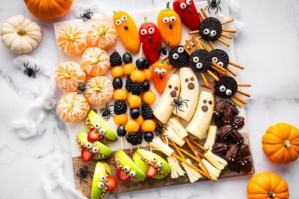 Halloween snack board featuring fruit kabobs, apple monster mouths, banana ghosts, Oreo spiders, and clementine pumpkins.