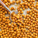Spoon scooping crispy roasted chickpeas from a baking sheet.