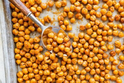 Spoon scooping crispy roasted chickpeas from a baking sheet.
