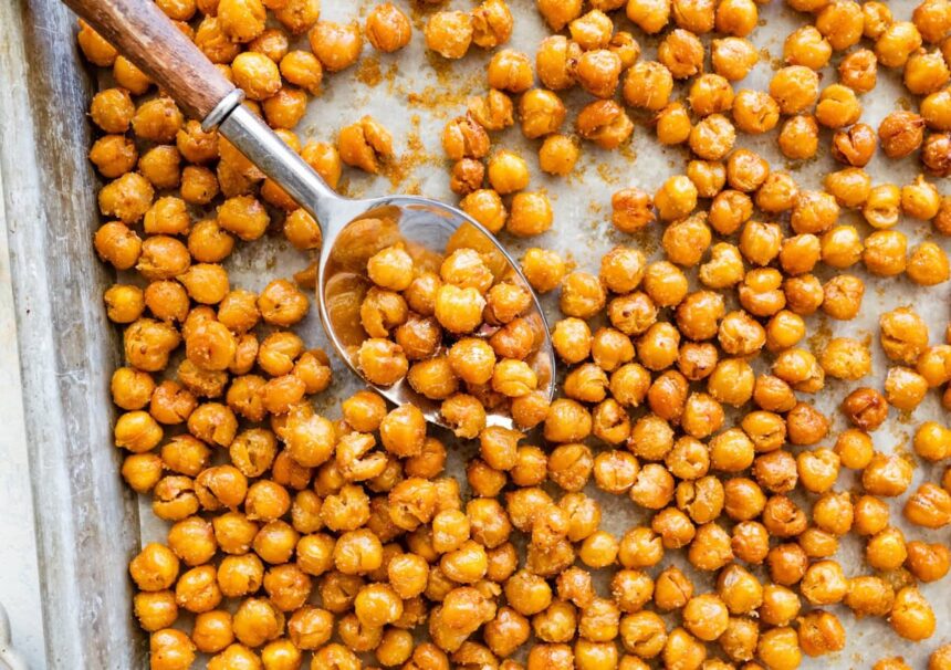 Spoon scooping crispy roasted chickpeas from a baking sheet.