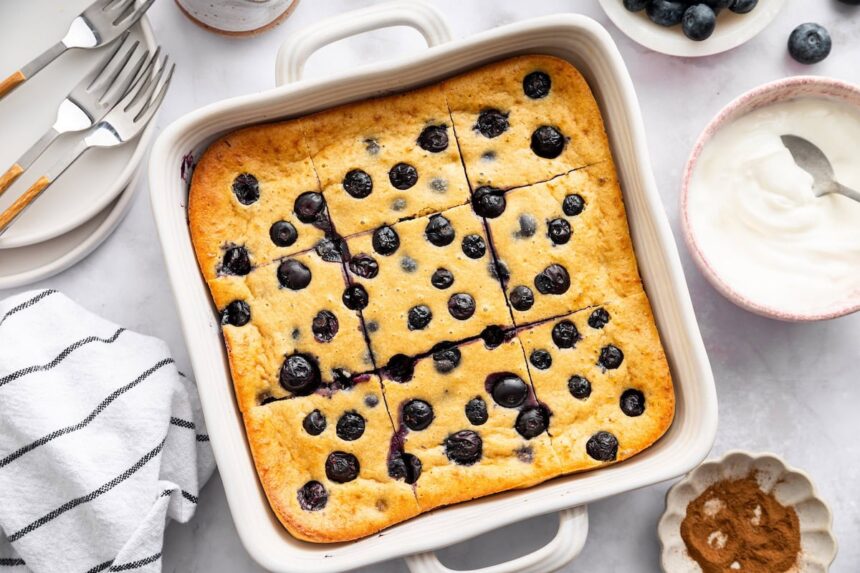 Golden blueberry cottage cheese breakfast bake sliced into pieces in a white ceramic baking pan.