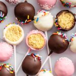 Chocolate, pink, and white cake pops decorated with sprinkles.