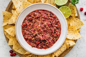 Bowl of cranberry salsa surrounded by tortilla chips and lime wedges, ready to serve.