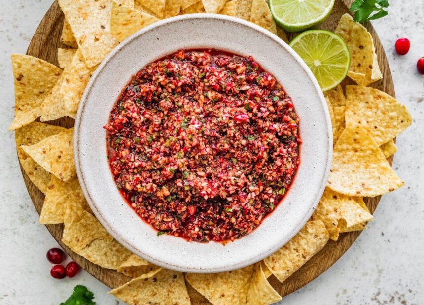 Bowl of cranberry salsa surrounded by tortilla chips and lime wedges, ready to serve.