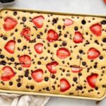Golden sheet pan pancakes with sliced strawberries and chocolate chips on a baking pan, ready to serve.