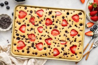 Golden sheet pan pancakes with sliced strawberries and chocolate chips on a baking pan, ready to serve.