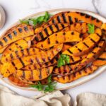 Grilled sweet potatoes on a white platter garnished with fresh parsley and served alongside a garlic aioli dip.