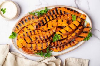 Grilled sweet potatoes on a white platter garnished with fresh parsley and served alongside a garlic aioli dip.