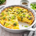 Crustless quiche with broccoli, cheese, onion, and a green onion garnish in a round baking dish with a slice removed.