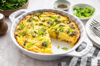 Crustless quiche with broccoli, cheese, onion, and a green onion garnish in a round baking dish with a slice removed.