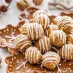 Plate of gingerbread protein balls with white chocolate drizzle arranged on a festive snowflake plate.