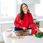Brittany in a red sweater smiling in the kitchen with a tray of gingerbread cookies in front of her.