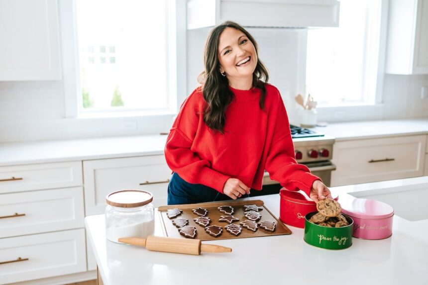 Brittany in a red sweater smiling in the kitchen with a tray of gingerbread cookies in front of her.
