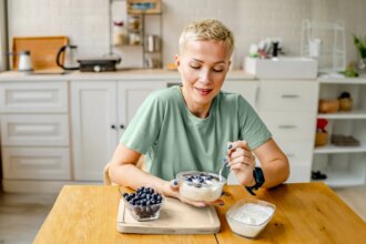 woman eating yogurt with blueberries in kitchen