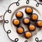 Finished high-protein buckeyes displayed on a white decorative plate with chocolate bottoms showing.