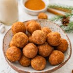 Close-up bowl of snickerdoodle protein balls with cinnamon sugar and milk in the background.