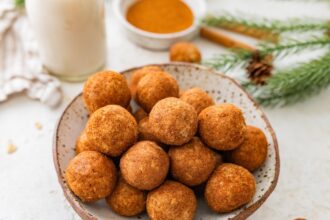 Close-up bowl of snickerdoodle protein balls with cinnamon sugar and milk in the background.