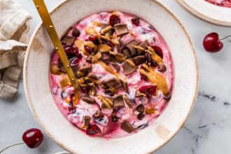 Close-up of chocolate cherry cheesecake yogurt bowl with crunchy toppings.