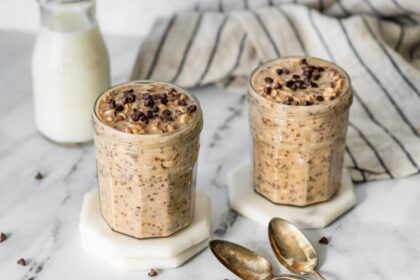 Two jars of cookie dough overnight oats with chocolate chips and spoons nearby.