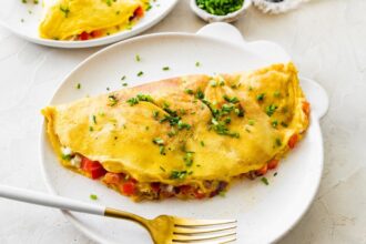 Cooked cottage cheese omelette on a white plate topped with chives served with a fork.