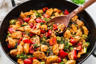 Close-up of kung pao chicken with bell peppers and broccoli being stirred.