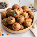 Bowl of monster cookie protein balls made with oats, peanut butter, chocolate chips, and M&M&rsquo;s.