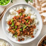 Thai basil chicken spooned over rice with fresh basil and green onions sprinkled on top.