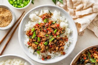 Thai basil chicken spooned over rice with fresh basil and green onions sprinkled on top.
