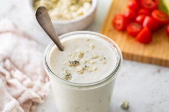 A glass jar of Greek yogurt blue cheese dressing with crumbled blue cheese pieces on top.