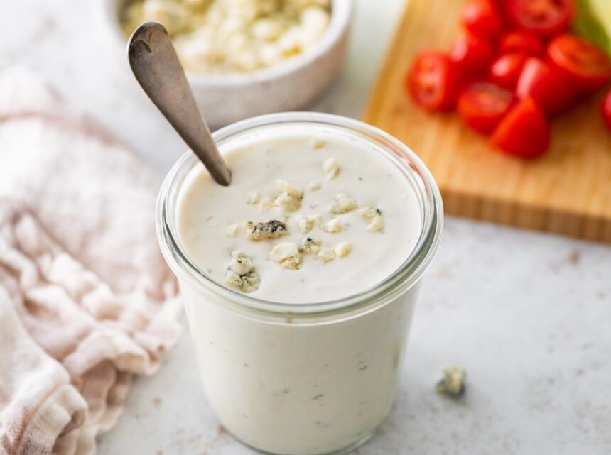 A glass jar of Greek yogurt blue cheese dressing with crumbled blue cheese pieces on top.