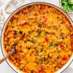 Enchilada pasta in a Dutch oven topped with melted cheese and fresh cilantro.