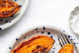 Three oven roasted sweet potato halves on a blue and white speckled plate sprinkled with flaky sea salt.